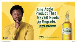 Yellow advert with a man in a mustard sweater on the left and a Savanna Dry cider bottle on the right, featuring the slogan 'One Apple Product That NEVER Needs An Upgrade.'