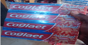 Stack of Colgate ActivGel toothpaste boxes being held, showing blue and red packaging with the Colgate logo and ActivGel label.