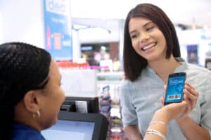 24 April - Business Strategy – African Marketing Confederation – African Marketing Confederation Smiling customer at checkout showing digital ClubCard barcode on smartphone to the cashier nearby.