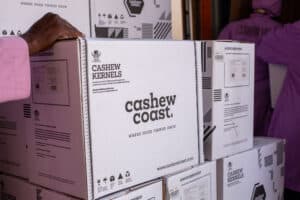 Boxes labeled Cashew Coast being stacked, with a person in a pink sleeve touching the top box, in a warehouse setting.