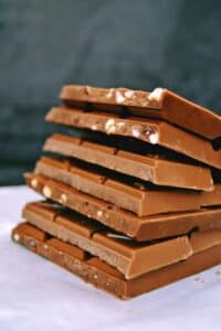 Stack of milk chocolate bars stacked on a white surface, with visible nuts and nougat bits.
