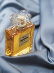 Chanel No.5 perfume bottle with amber liquid resting on blue satin fabric, close-up view of the crystal cap and label