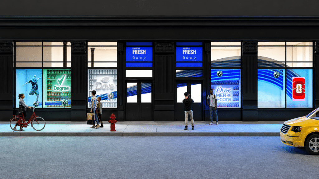 Urban storefront with large blue advertising windows, pedestrians on the sidewalk, and a yellow taxi at right edge—nighttime street scene