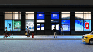 Urban storefront with large blue advertising windows, pedestrians on the sidewalk, and a yellow taxi at right edge—nighttime street scene