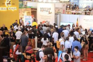 Crowded exhibition hall with multiple coffee booth displays, including Uganda Coffee and Black Knight signage.