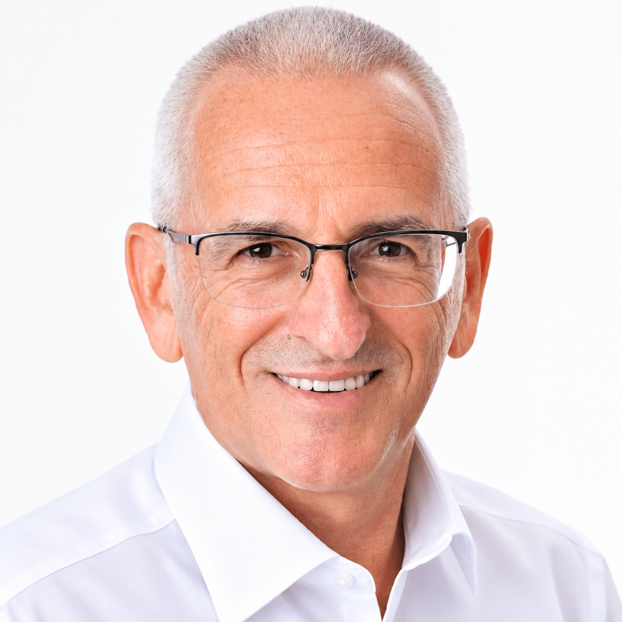 Portrait of a smiling older man with gray hair and rectangular glasses wearing a white shirt, facing the camera.