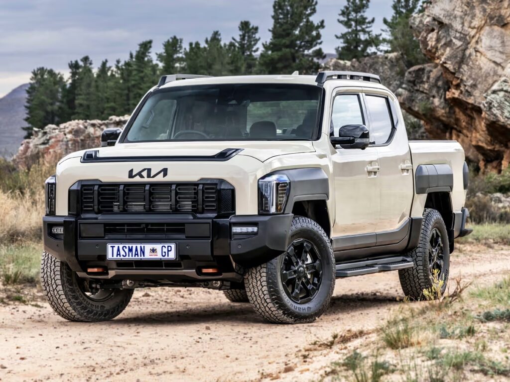 Beige off-road pickup truck parked on a dirt trail with rocky hills and pine trees in the background