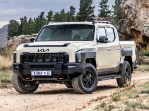 16 July - Advertising – African Marketing Confederation – African Marketing Confederation Beige off-road pickup truck parked on a dirt trail with rocky hills and pine trees in the background