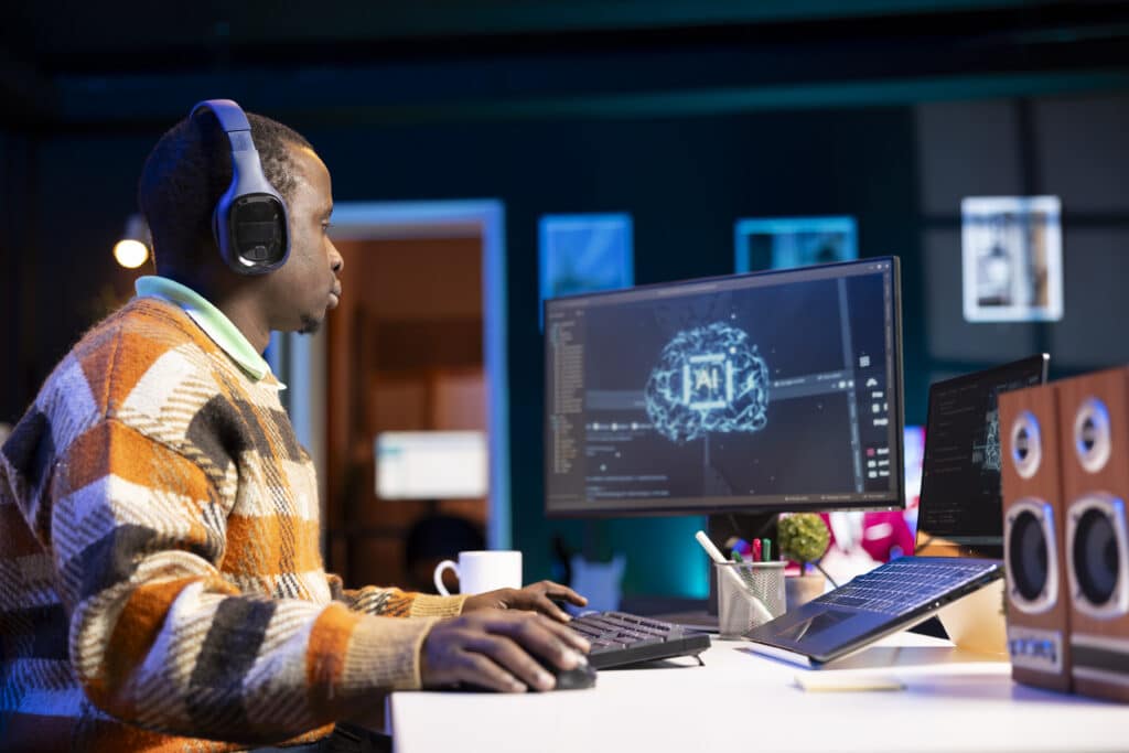 Person wearing blue over-ear headphones at a desk with multiple monitors showing digital graphics, focused on work.