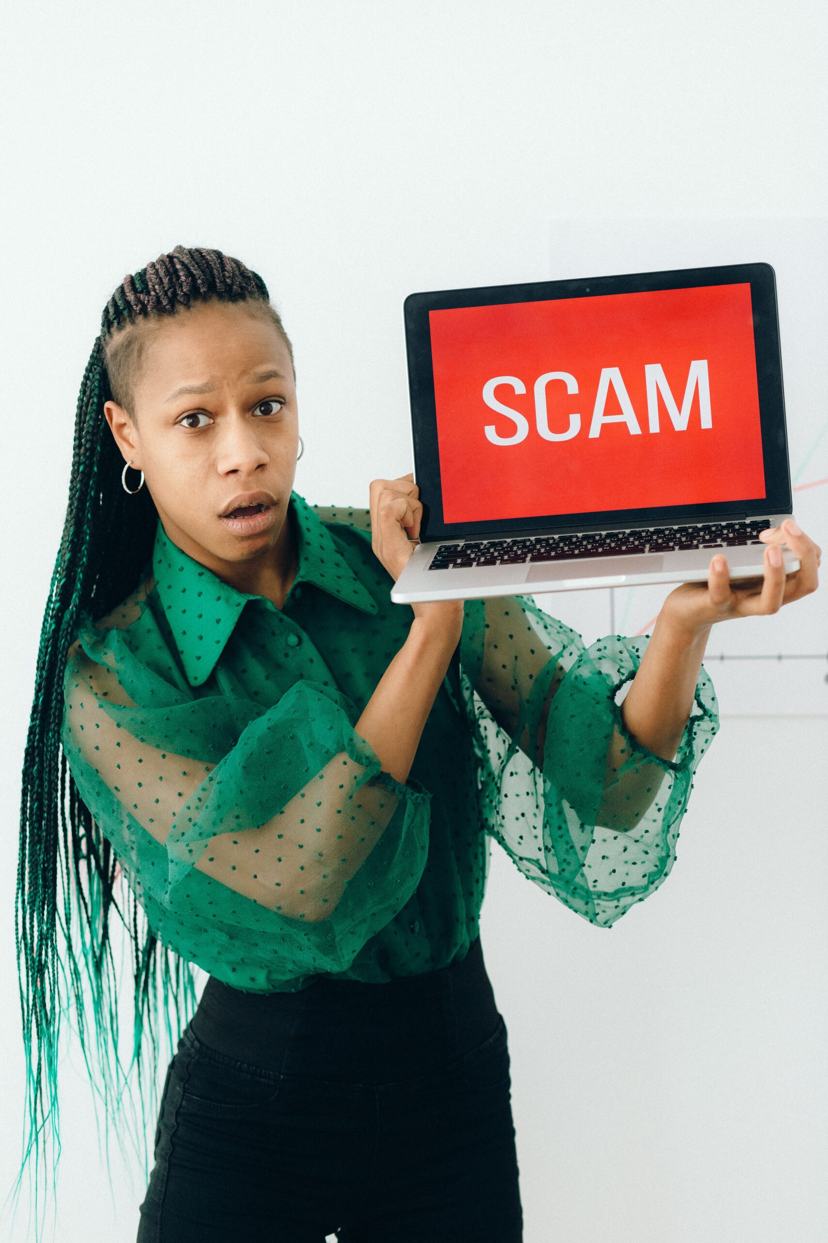29 July - Brand Phishing – African Marketing Confederation – African Marketing Confederation Woman with surprised expression holds laptop showing a red screen reading 'SCAM'.