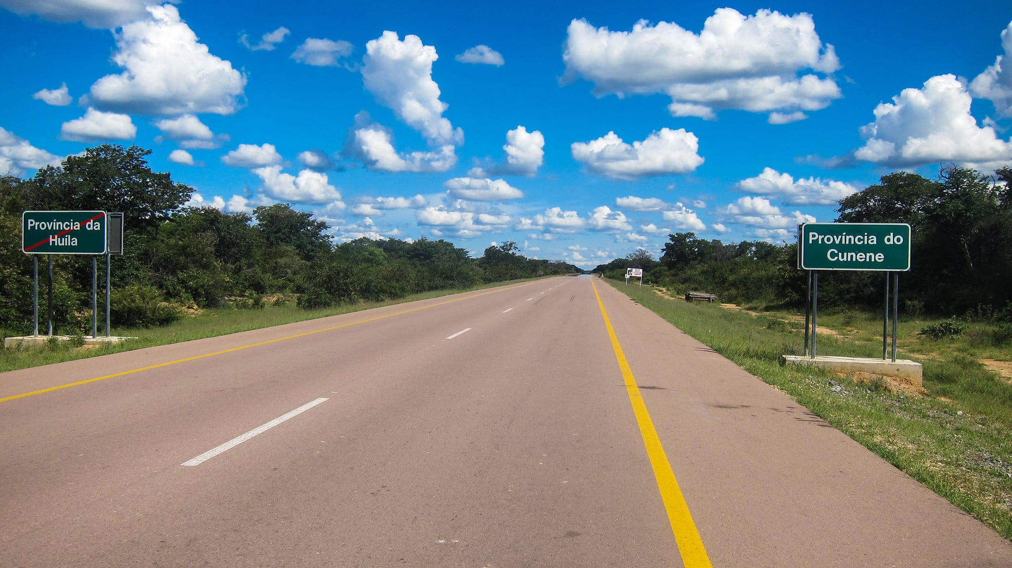 30 July - Supply Chain – African Marketing Confederation – African Marketing Confederation Two green provincial-border signs mark the road crossing between Huila (left) and Cunene (right) provinces under a blue sky with scattered clouds in a rural setting.