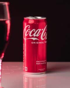 7 July - Cola Wars – African Marketing Confederation – African Marketing Confederation Red Coca-Cola can on a glossy surface with a subtle reflection against a dark background