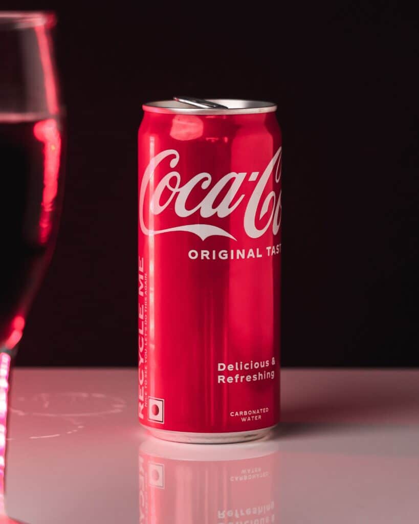 Red Coca-Cola can on a glossy surface with a subtle reflection against a dark background