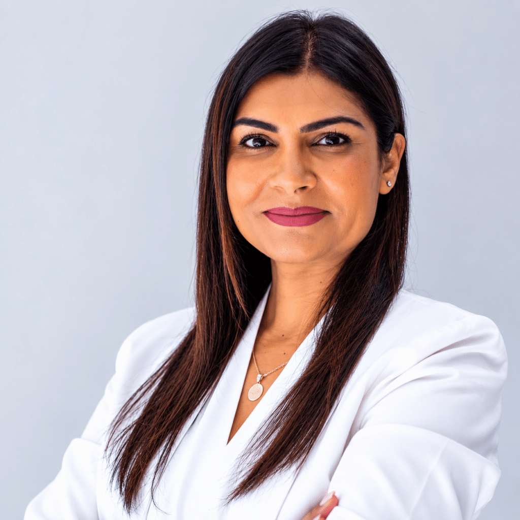 Professional portrait of a woman with long dark hair in a white blazer, against a light gray background, smiling subtly.