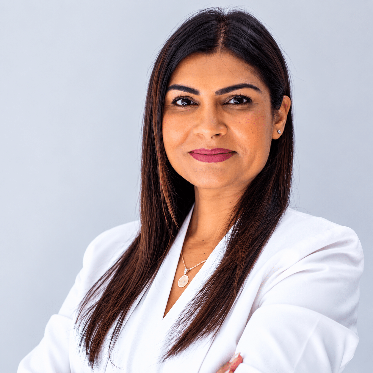 Professional portrait of a woman with long dark hair in a white blazer, against a light gray background, smiling subtly.