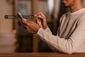 Person using a smartphone with a dark translucent search bar overlay showing a magnifying glass icon and the word 'Search...' in white text.