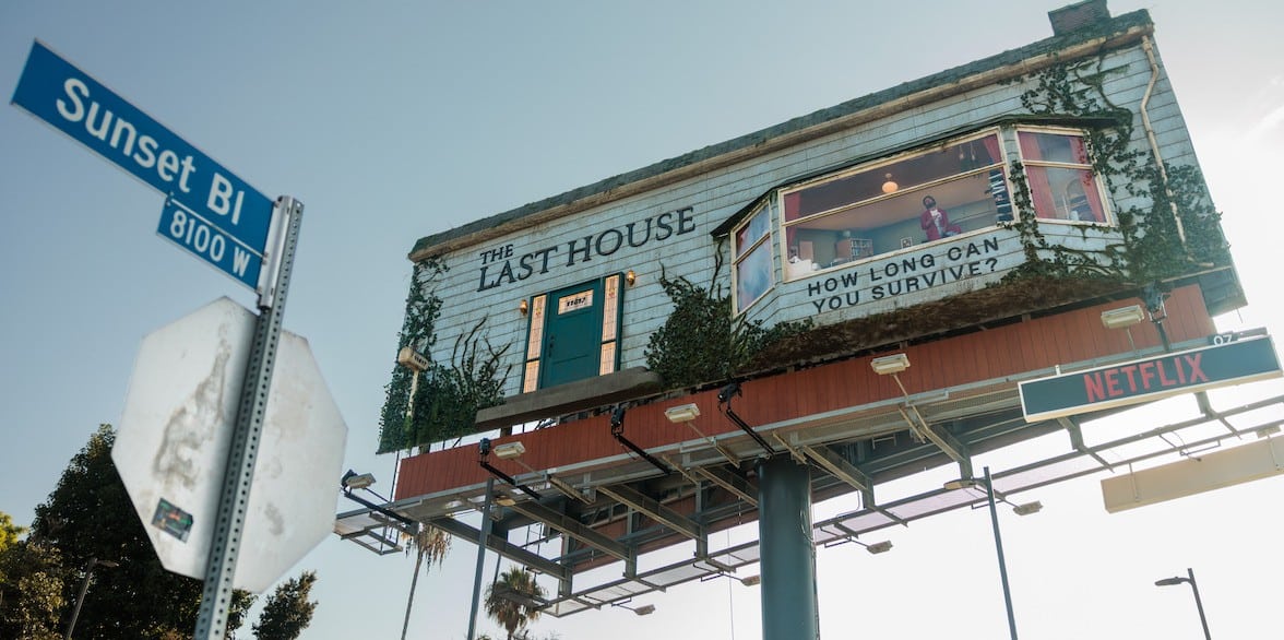 A large billboard atop a highway overpass advertising 'The Last House' with a 'How long can you survive?' window display and a Netflix sign below.