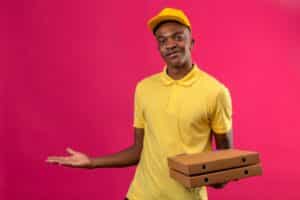 August Consumer Behaviour Delivery worker in a yellow polo and cap holds three stacked cardboard boxes against a bright pink background