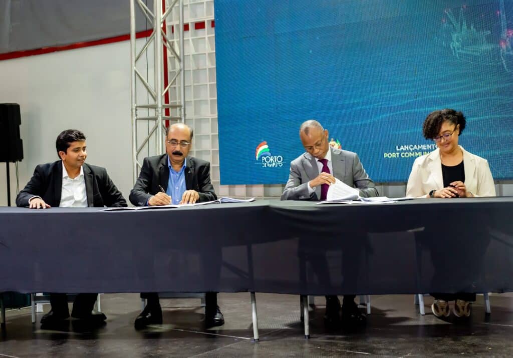 Panel of four professionals seated at a long table, signing documents, with a blue digital backdrop displaying a Porto News logo behind them.