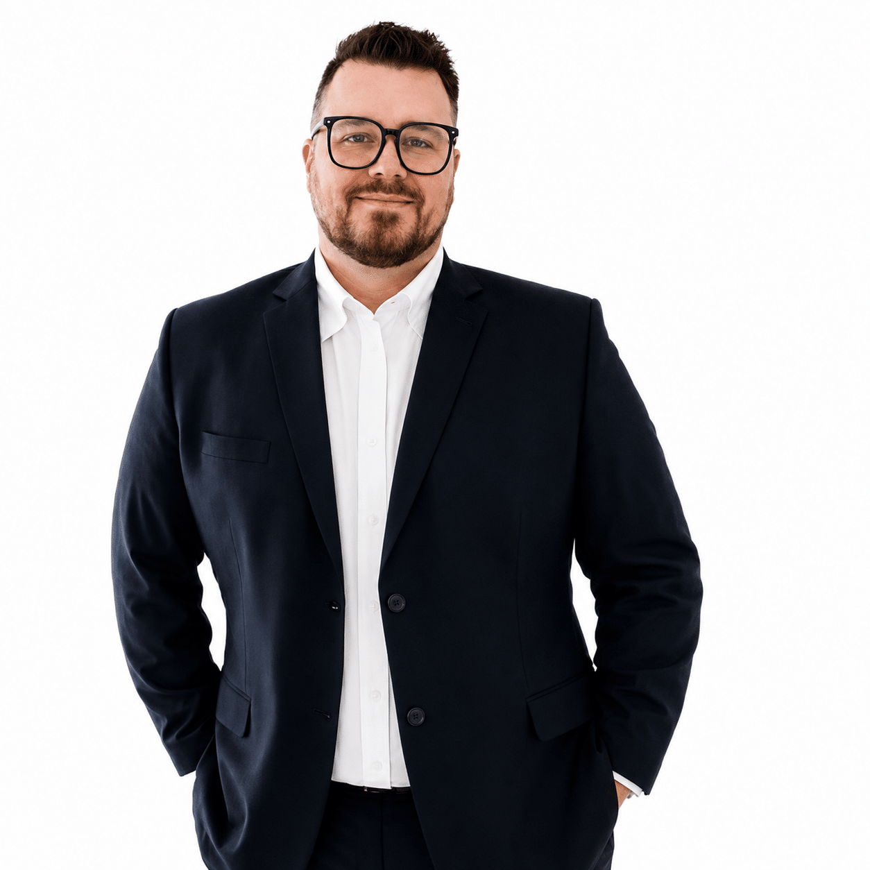Portrait of a man in a navy suit and white shirt, wearing glasses, with hands in pockets and a confident smile.