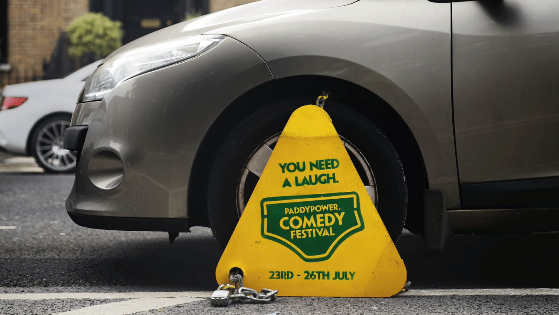 6 August - Guerrilla Marketing – African Marketing Confederation – African Marketing Confederation Yellow triangular sign in front of a parked silver car promoting Paddy Power Comedy Festival (23–26 July).
