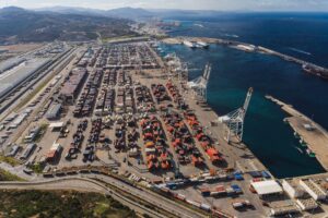 Aerial view of a busy container port with rows of stacked cargo containers, large cranes, and ships along the dock.