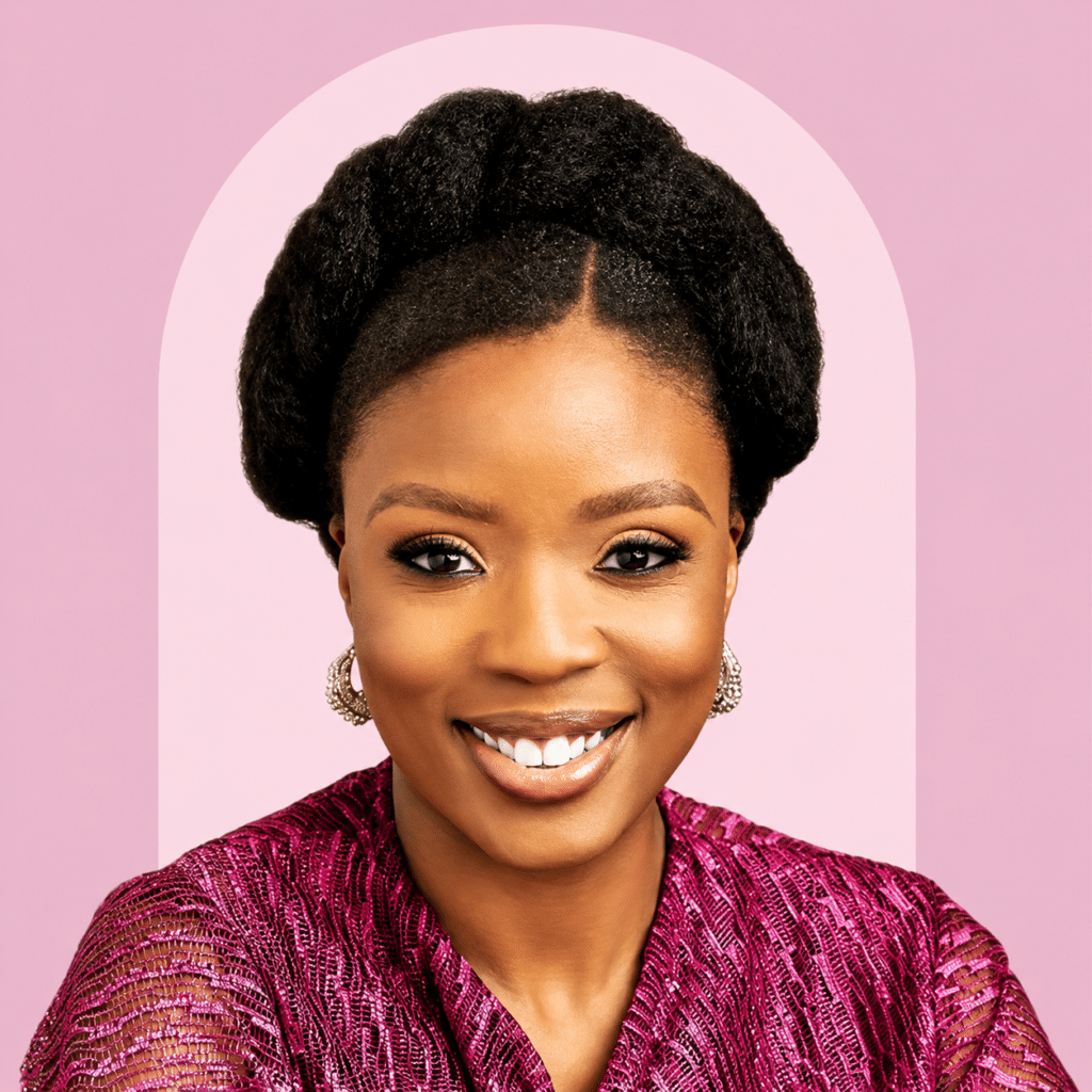 Smiling woman with braided updo and gold earrings, wearing a pink textured top against a pink background.