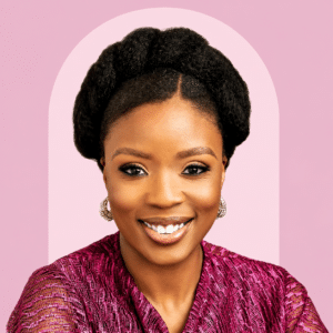 September Marketing Talent Smiling woman with braided updo and gold earrings wearing a pink textured top against a pink background