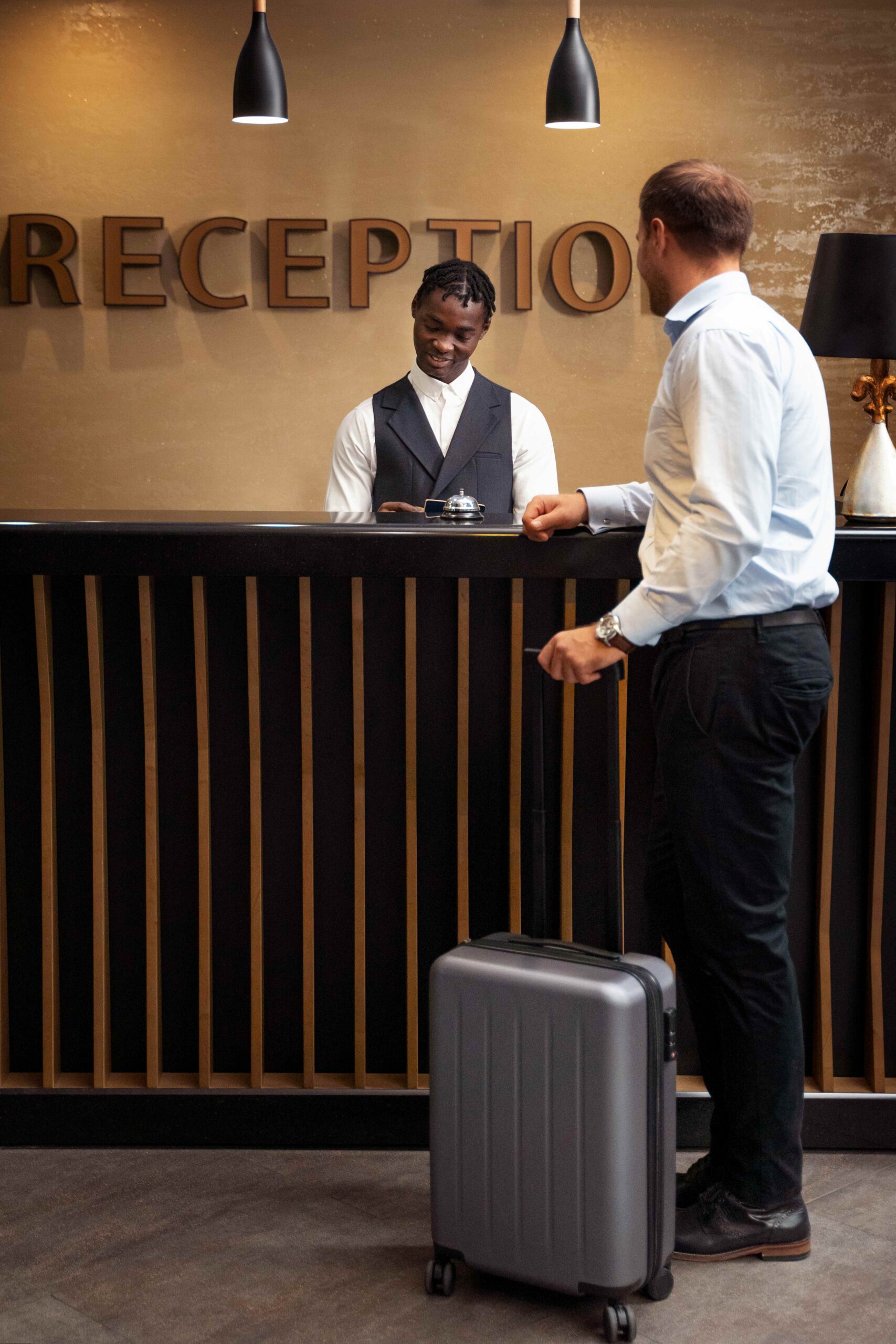 Hotel receptionist assisting a guest at the check in counter with a gray suitcase nearby behind the desk