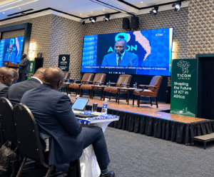 September Conference Conference hall stage with a man in a blue suit speaking at a podium on a large screen ticon africa banner visible'shaping the future of ict in africa'