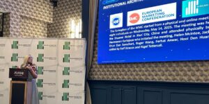Woman at a podium giving a talk avani sign backdrop with african marketing confederation logos large blue conference slide screen behind her
