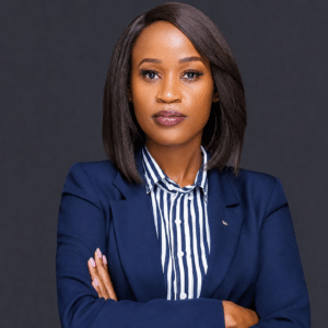 September Marketing Talent Professional portrait of a woman with straight shoulder length hair wearing a navy blazer and striped shirt arms crossed against a dark background