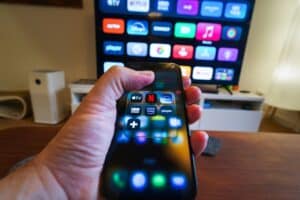 Person holding two smartphones with app icons visible on their screens a large tv screen in the background shows colorful app icons