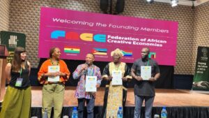 Five people on stage holding certificates at an event for the federation of african creative economies with a pink backdrop banner behind them