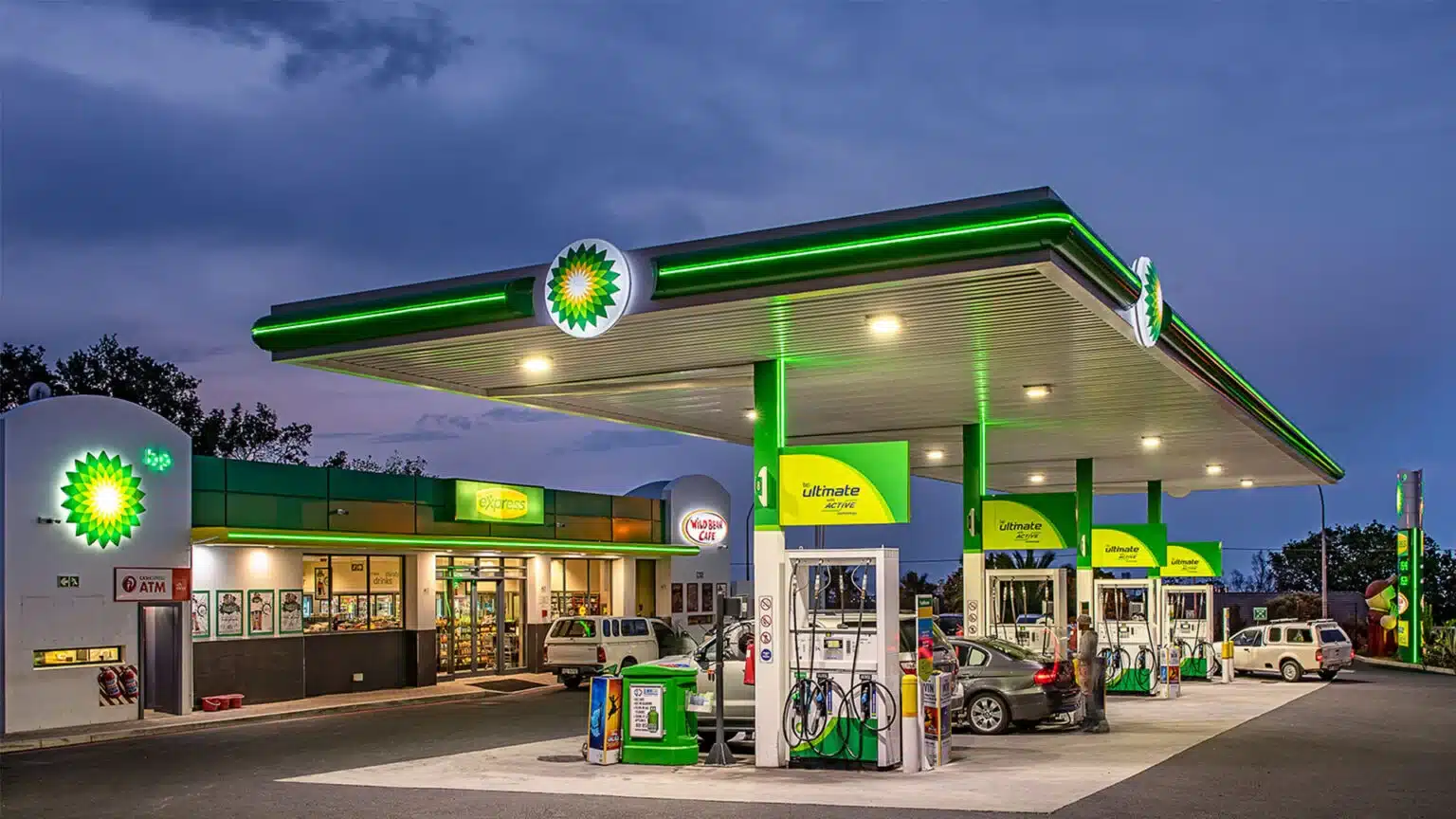 Bp gas station at dusk with green canopy pumps and a convenience store showing the wild bean cafe sign
