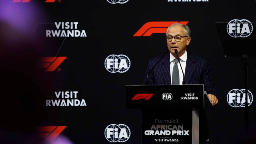 Speaker at a Formula 1 event podium with FIA logos and 'Visit Rwanda' branding.
