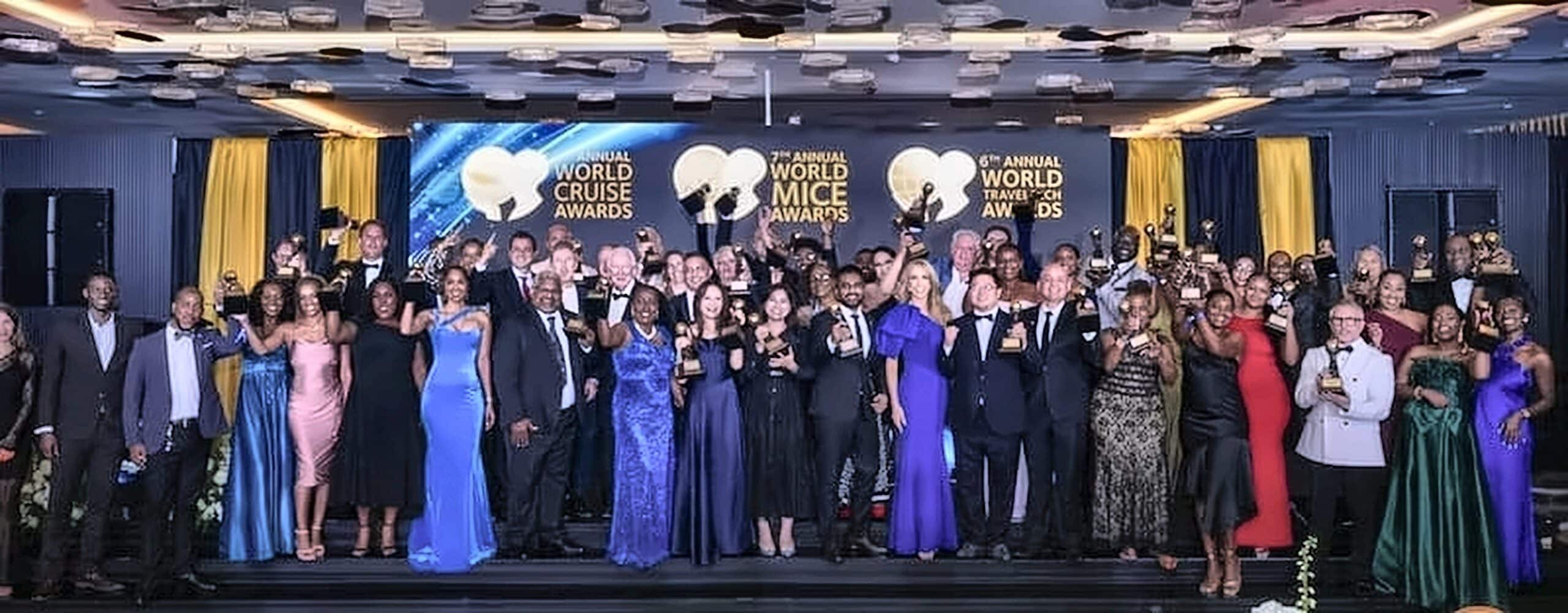 Group of formally dressed award winners posing on stage with trophies at the world cruise awards ceremony