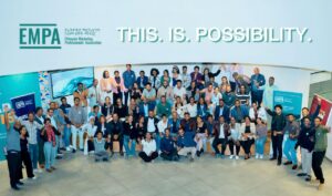 Diverse group of people posing for a group photo in a bright lobby under an empa banner with 'this is possibility ' text above