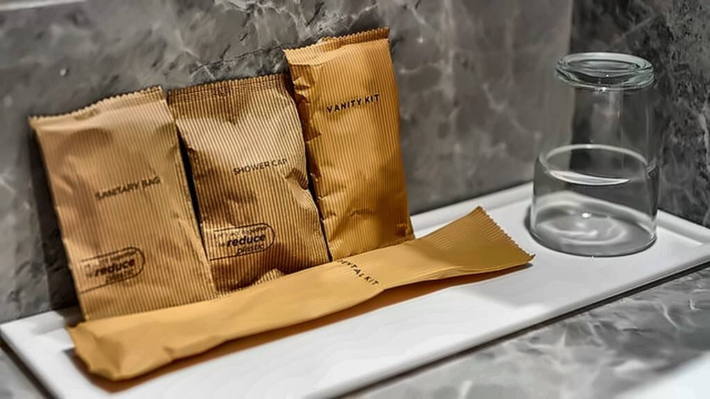 Gold hotel toiletries sachets arranged on a marble bathroom counter, including a vanity kit and shower gel beside a glass.