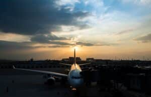 A passenger jet at a gate viewed from the nose with a sunset sky and dark clouds in the background