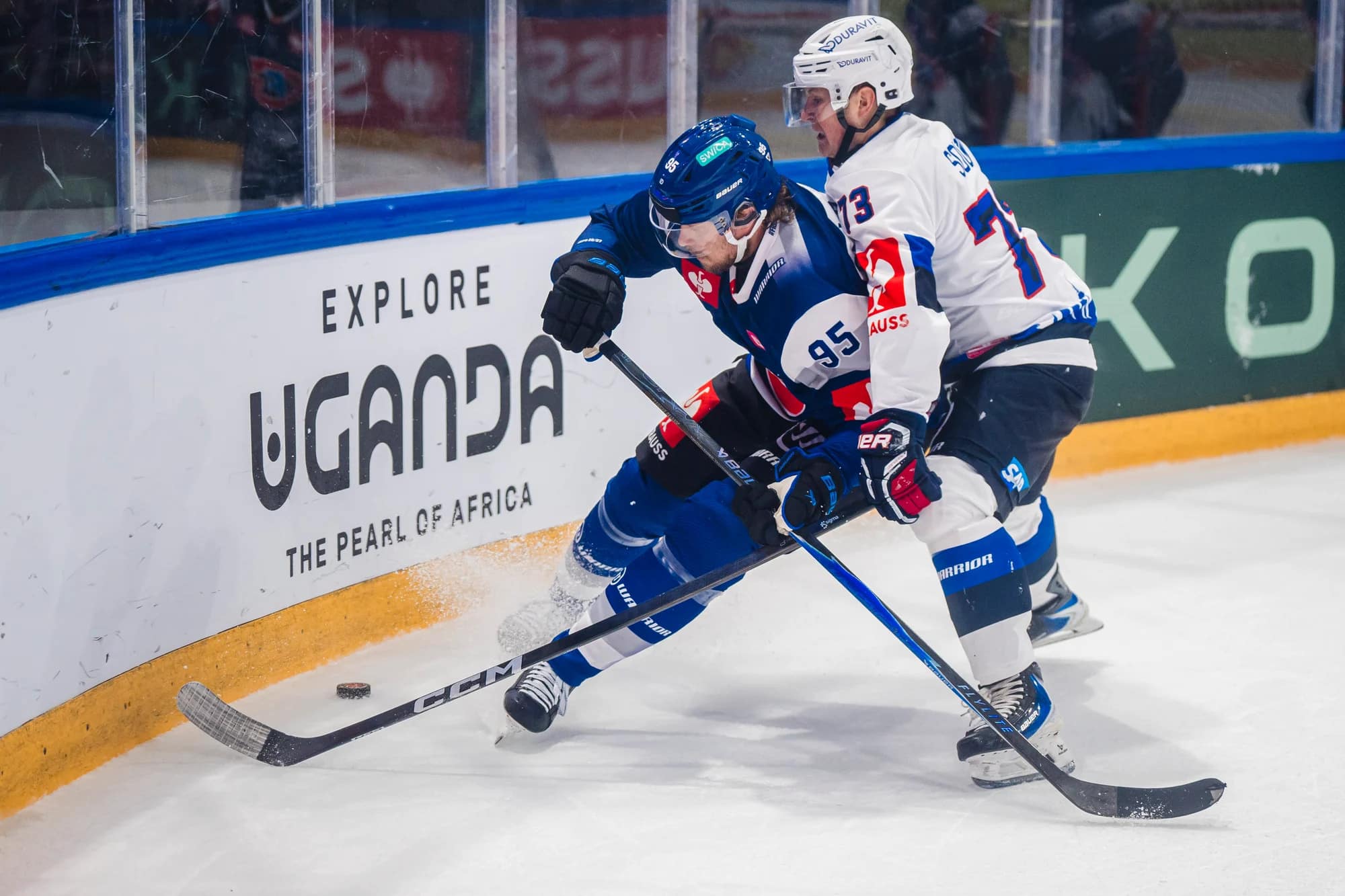 Two hockey players battle for the puck along the boards during a game one in blue and one in white