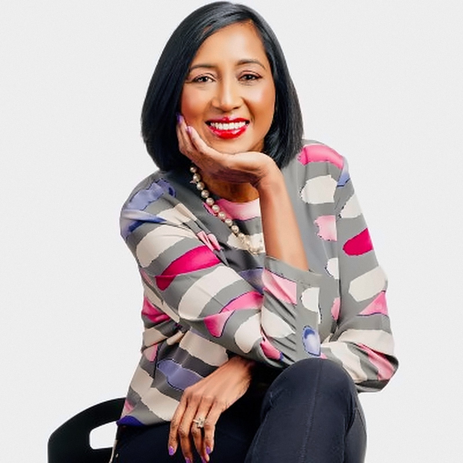 Smiling woman with short dark hair resting her chin on her hand wearing a colorful geometric blouse