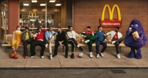 October Sports Marketing Group of men in athletic wear sit on a bench outside mcdonald's with ronald mcdonald and grimace mascots nearby enjoying snacks and drinks