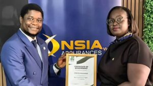 Two professionals stand side by side as one hands a framed certificate of achievement to the other with a blue nsia banner in the background